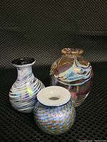 Three miniature art glass vases grouped together on black textured background.