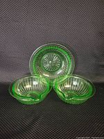 Three uranium glass ribbed bowls, two smaller with pouring spouts and one larger without spout, glowing green under light.