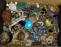 Top-down photo showing a dense collection of costume jewelry including necklaces, pendants, brooches with varied styles and colors.