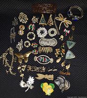 Full lot of approx 40 pieces of costume jewelry, shown on dark textured background, mostly brooches and earrings with floral, Christmas, insect and geometric designs.