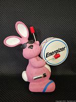 Front view of the pink Energizer Bunny resin bank holding a drum with the Energizer logo, wearing black sunglasses, with a visible battery detail on its side.