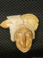 Stone carving of an Indigenous American Iroquois face with carved feathers, showing front view and detail of facial features and markings.