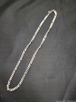 Full view of 18 inch sterling silver Figaro chain laid flat on black fabric background.