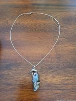 Full view of the pendant and chain laid on wooden surface showing the complete necklace.