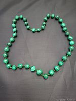 Full view of malachite beaded necklace arranged on black surface showing overall length and bead count.