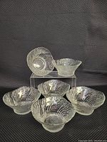 Six clear textured glass bowls with embossed swirling tree branch patterns, arranged in a group on a black textured surface.
