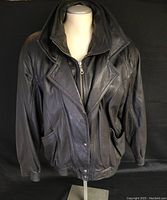 Front view of men's black leather bomber jacket on a mannequin showing double collar and elastic waistband.