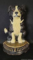 Front view of sitting Border Collie doorstop showing detailed black and white painted fur and glass eyes on a round decorative base.