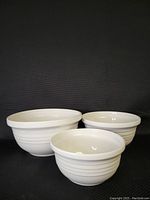 Three white pottery mixing bowls arranged side by side, showing graduated sizes and glossy finish.
