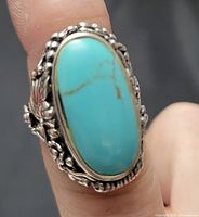 Close-up front view of the ring highlighting the oval turquoise stone and floral bezel setting.