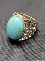 Front side view of ring showing large oval raised turquoise stone and leaf lattice band design
