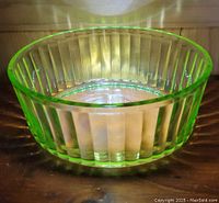 Green uranium glass ribbed oval refrigerator dish shown from an angle highlighting the ribbed vertical pattern and translucent green tint.