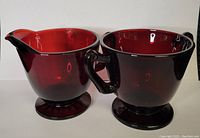 Photo showing the two ruby red glass pieces side by side, cream pitcher with spout and sugar bowl with one handle visible.