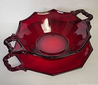 Top perspective view showing ruby red serving dish with two handles resting inside the matching under plate, highlighting the glossy finish and octagonal shape.