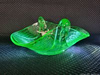 Front angled view of green uranium glass sparrow handled candy dish illuminated to show glowing effect and detailed feather patterning.