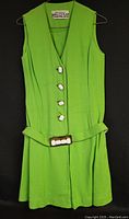 Full view of the sleeveless kelly green mini dress hanging on a hanger showing front buttons and belt.
