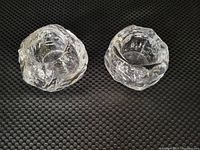 Top view of two clear crystal votive candle holders with textured snowball design placed side by side on black surface.