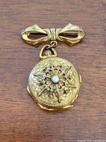 Front view showing bow accent and closed locket with ornate design and central pearl.