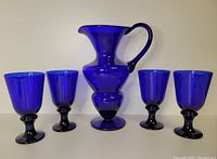 Full set of one cobalt blue glass water jug and four matching goblets displayed side by side.