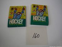 Two unopened 1990-91 OPC hockey card wax packs sitting side by side with a number card '160' in front.