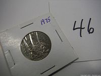 Front side of the 1975 Canadian half dollar coin in a white cardboard coin holder with staples and marked '1975'.
