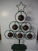 Front view of the green metal Christmas tree frame with six rusted jingle bells inside circular loops and a star topper.