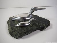 Photo showing two polished metal loon sculptures on dark green stone base, viewed from a front angle.