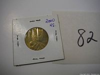 Front (obverse) side of 2000 Sacagawea dollar coin showing Sacagawea with infant, in protective 2x2 cardboard holder with clear plastic.