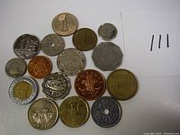 Top-down photo showing 16 vintage coins arranged on a white surface with a note featuring four vertical black lines.