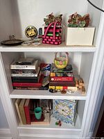 Shelf with assorted books, backgammon game box, dice, and wooden blocks alongside figurines and small collectibles
