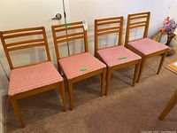 Four wood frame dining chairs with upholstered seats in pink and white zigzag pattern, lined up side by side showing condition and design