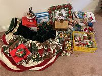 Wide view of assorted Christmas decorations showing folded tree skirts, boxes of lights, multiple plush and ceramic ornaments, and fabric items.