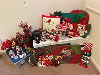 Wide shot of various Christmas decor including cushions, floral arrangements, decorations, and decorative mats arranged on a white radiator cover and blue table.