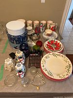 View of Christmas themed plates, bowls, cups, tin boxes, candles, and various decorative items arranged on a table.