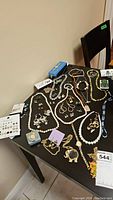Overview of jewelry lot showing necklaces, watches, earrings, and boxed items on black table