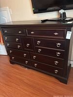 Full view of dark wooden dresser with 10 drawers, metal hardware, on wooden floor.