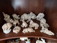 Wide angled photo showing all 12 vintage elephant figurines arranged on a curved wooden shelf.