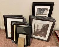 Group of various wood, metal and plastic picture frames in black and brown tones. Some frames have New York City themed prints and mat board inside. Frames vary in size from 7x4 to approximately 10.5x23 inches.