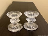 Pair of Iittala Festivo glass candle holders with clear textured glass and rounded design seen side by side on a wood surface.