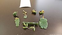 Overview of six jade jewelry pieces: pendants, brooch, and pair of earrings, displayed on table.