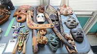 Overview of lot showing multiple hand carved wood masks, terra cotta mask, clay mask, small shell mask, and hand painted boomerang.