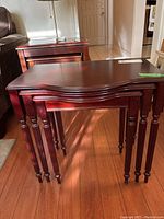 Three dark polished wooden nesting tables stacked inside one another, showing turned legs and curved tops.
