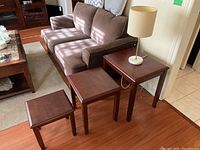 Three wooden nesting tables arranged in front of a couch on a wood floor.