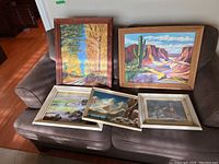 Five framed artworks on sofa showing a variety of landscapes and a print, giving overall view of lot composition