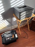 Both printers placed on wooden floor, Brother printer on small table and Epson printer on floor.