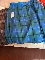 Two ladies wool kilts are shown folded on a surface; one kilt is brown plaid and the other is blue and green plaid tartan pattern.