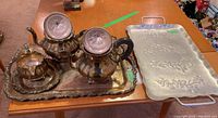 Silver plate coffee pot, teapot, sugar bowl, creamer on ornate silver plate tray next to floral motif metal tray
