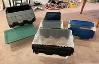 Array of different GBC plastic storage bins with black, green, clear, and blue lids, plus insulated tote bag visible in the background.