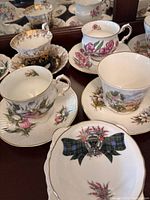 Photo showing assorted teacups and saucers with floral designs and a provincial crest on one saucer.