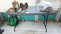 Grey plastic utility table with black metal folding legs. The table is 48x24x24 inches. Various items and bags on top of the table are not included.
